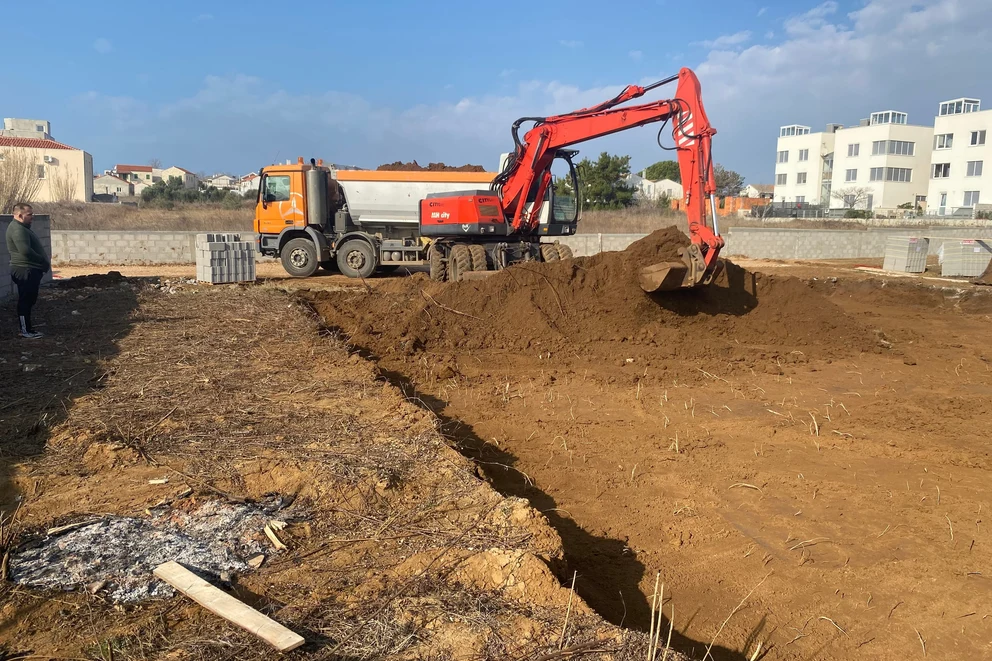 Bager kopa temeljni rov i istresa zemlju u kamion kiper na gradilištu